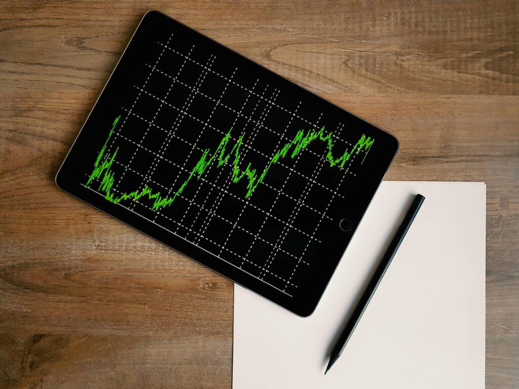 Flatlay of an iPad displaying stock market graph on a wooden desk with a pencil and paper.